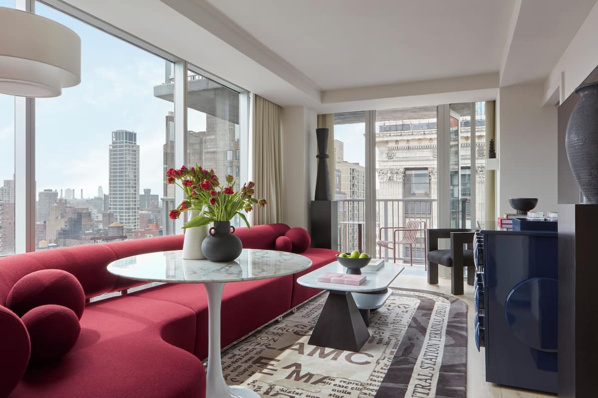Una sala de estar moderna con un sofá rojo, una mesa redonda y vistas de la ciudad a través de amplios ventanales.