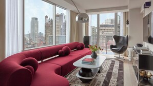 A modern living room with a red sectional sofa, a black armchair, a coffee table with books, and a view of the city through large windows.