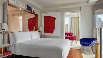 Una habitación de hotel moderna con una cama grande, una pared de acento roja, una silla roja y una silla azul.