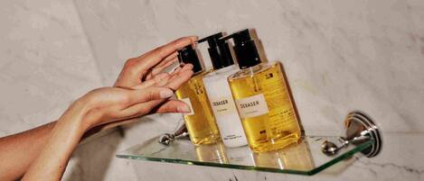A hand holding a bottle of Débasser on a glass shelf in a bathroom with marble walls.