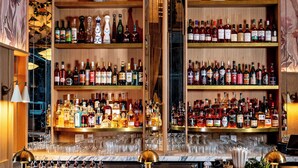A bar with multiple shelves of liquor bottles, a marble countertop, and bar stools. - Hotel Park Ave NYC (New York)