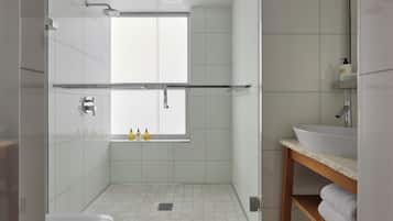 Un baño moderno con ducha de vidrio, un lavamanos blanco y una ventana sobre la ducha.
