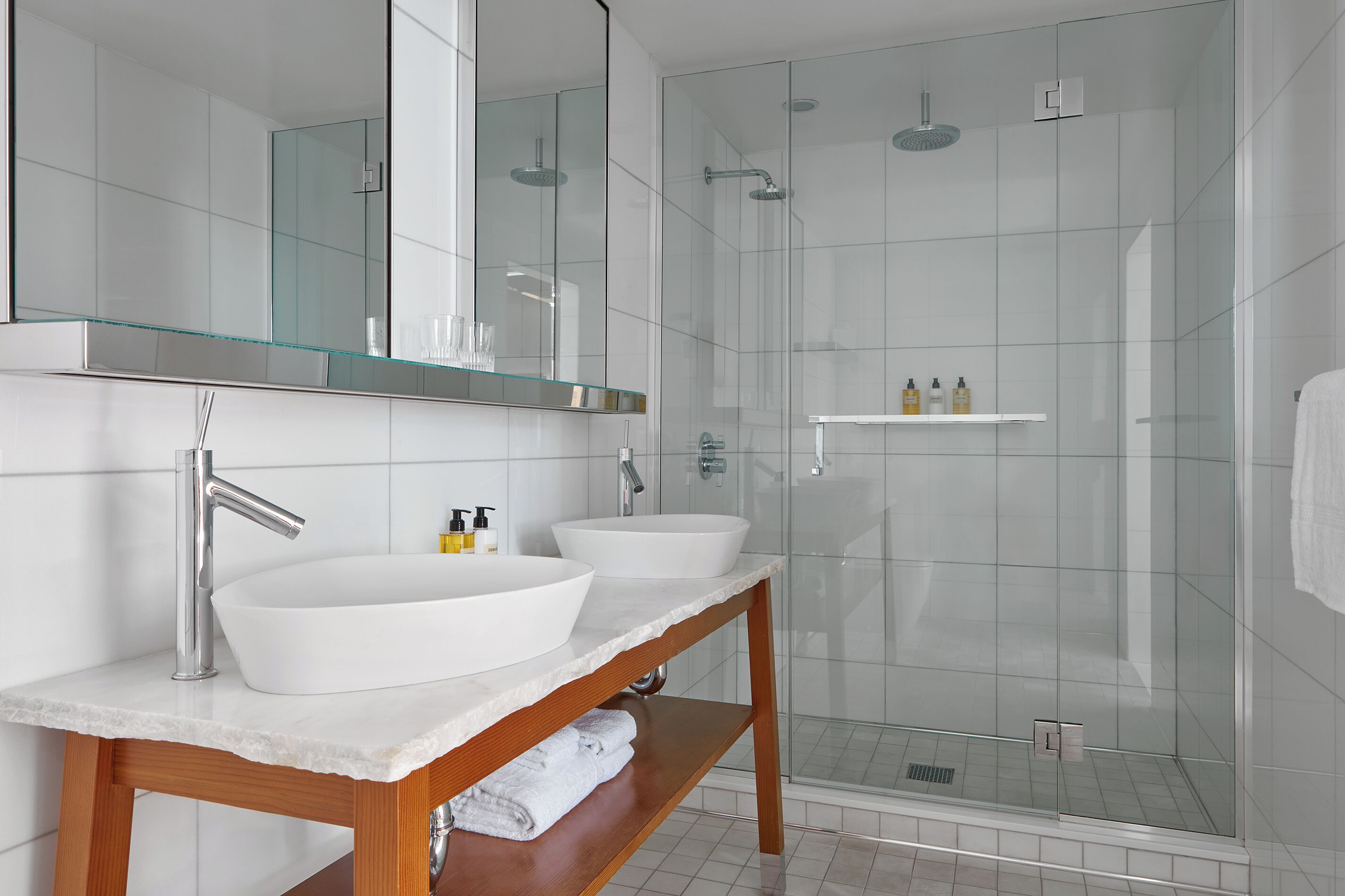Un baño moderno con dos lavamanos, un espejo grande y una ducha con mampara de vidrio.