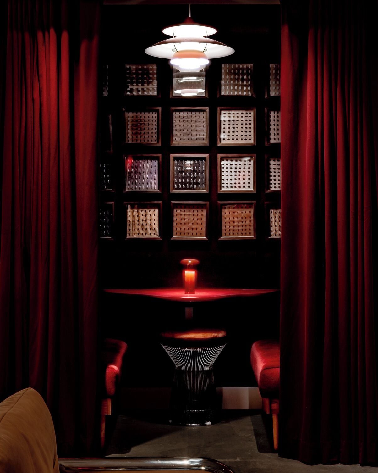 Een kamer in gedempt licht met rode gordijnen, een tafel en twee stoelen.
