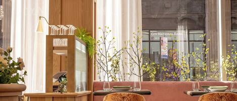 A cozy restaurant with wooden furniture, a bar area, and large windows with a city view.