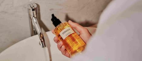 A person holding a bottle of DEBASER next to a bathroom sink with a mirror above it.
