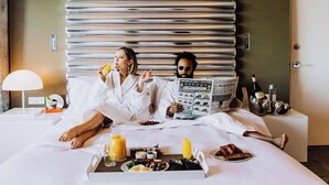 A hotel room with a large bed, a bedside table with a lamp, a tray with breakfast items, and a newspaper. - W Bellevue (Bellevue)