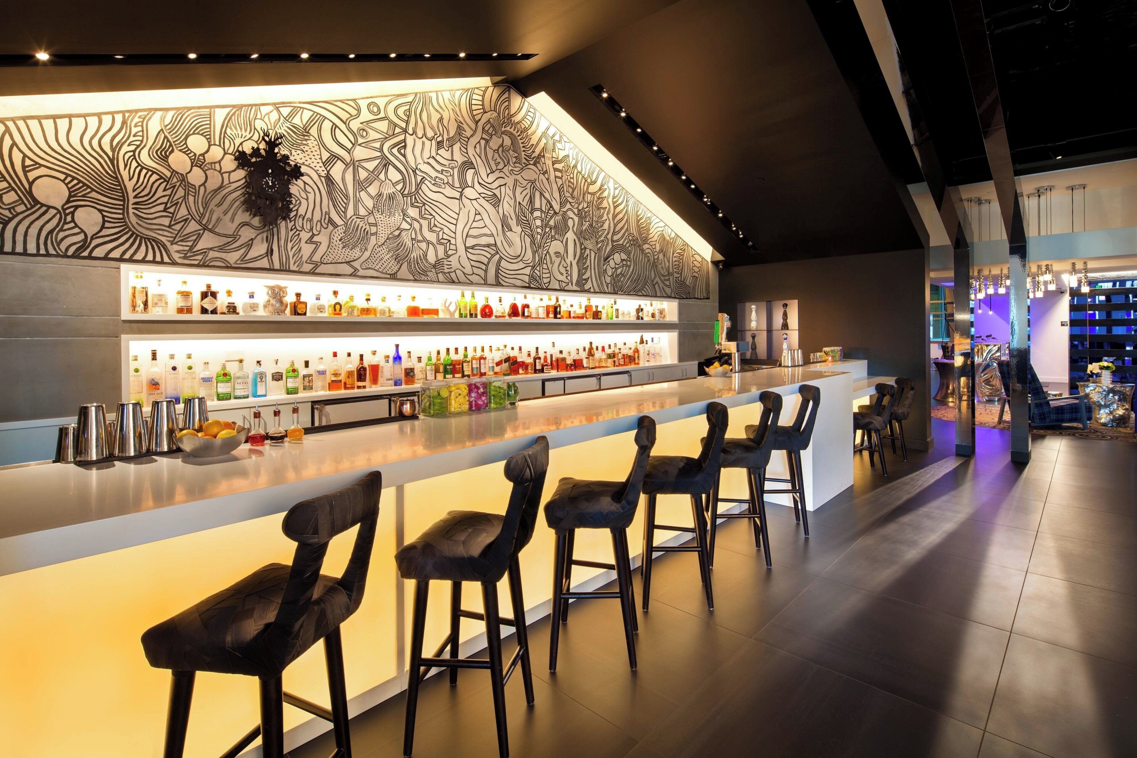 Un'area bar con un lungo bancone, diversi sgabelli e una parete decorativa.