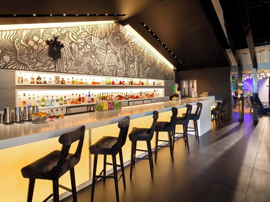 Un'area bar con un lungo bancone, diversi sgabelli e una parete decorativa.