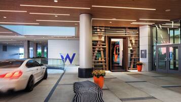 A modern hotel entrance with a white car parked outside, a large 'W' logo, and a seating area with a patterned bench.
