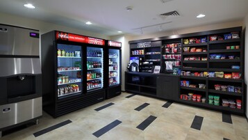 Un área de venta con dispensadores de bebidas refrigeradas, una máquina de café y estantes llenos de aperitivos y bebidas.