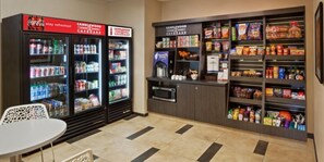 A snack bar with refrigerated beverage dispensers, a microwave, and shelves stocked with snacks and beverages.