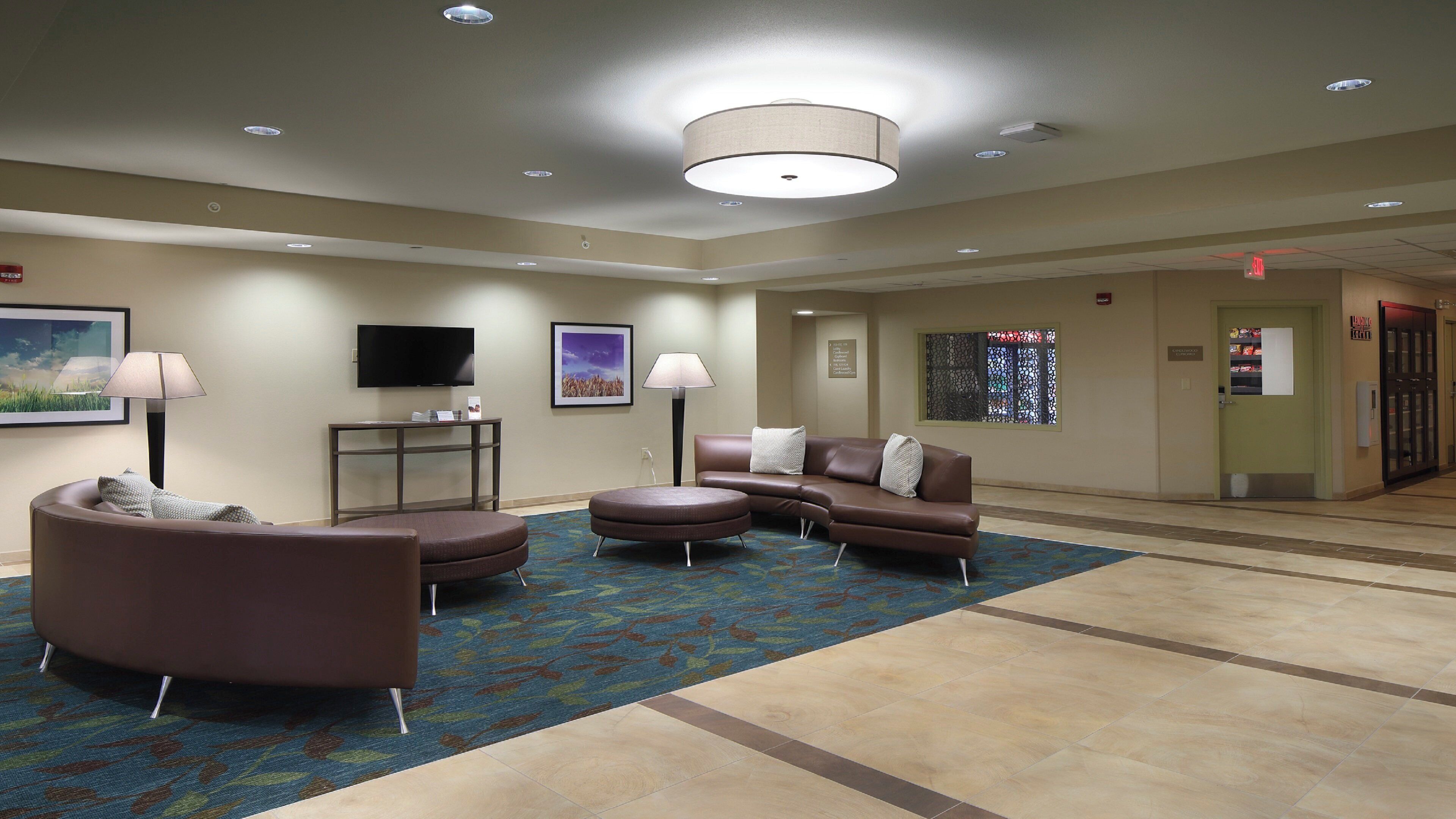 A hotel lobby with a seating area, a flat-screen TV, a large window, and a reception desk.