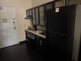 Una cocina compacta con un refrigerador negro, cafetera y microondas.