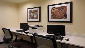 Un espacio de trabajo con dos escritorios, cada uno con monitor de computadora, teclado y ratón. Hay obras de arte enmarcadas en la pared sobre los escritorios.