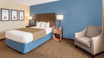 A hotel room with a large bed, two bedside tables with lamps, a chair, and three framed pictures on the wall.