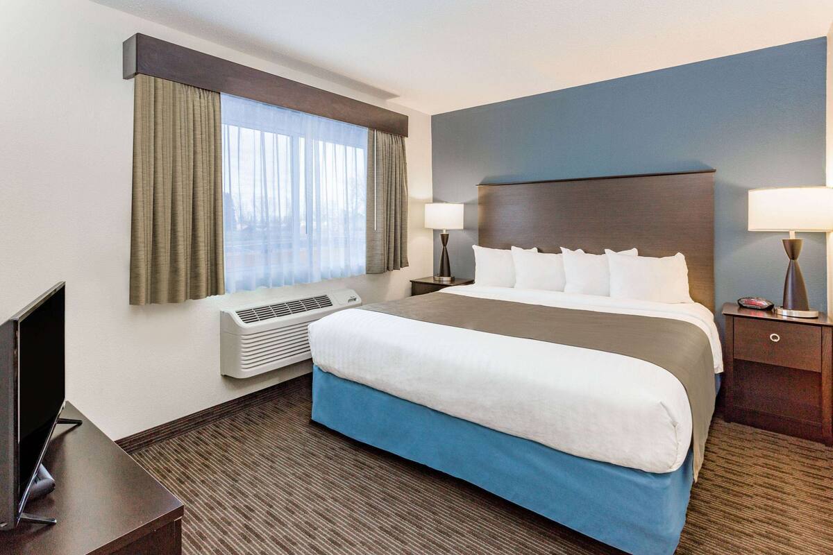 A hotel room with a large bed, a flat-screen TV, a desk, and a window with curtains.