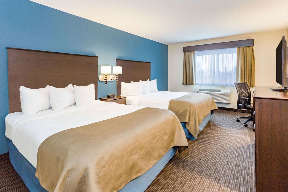 A hotel room with two beds, a desk, a chair, a TV, and a window with curtains.