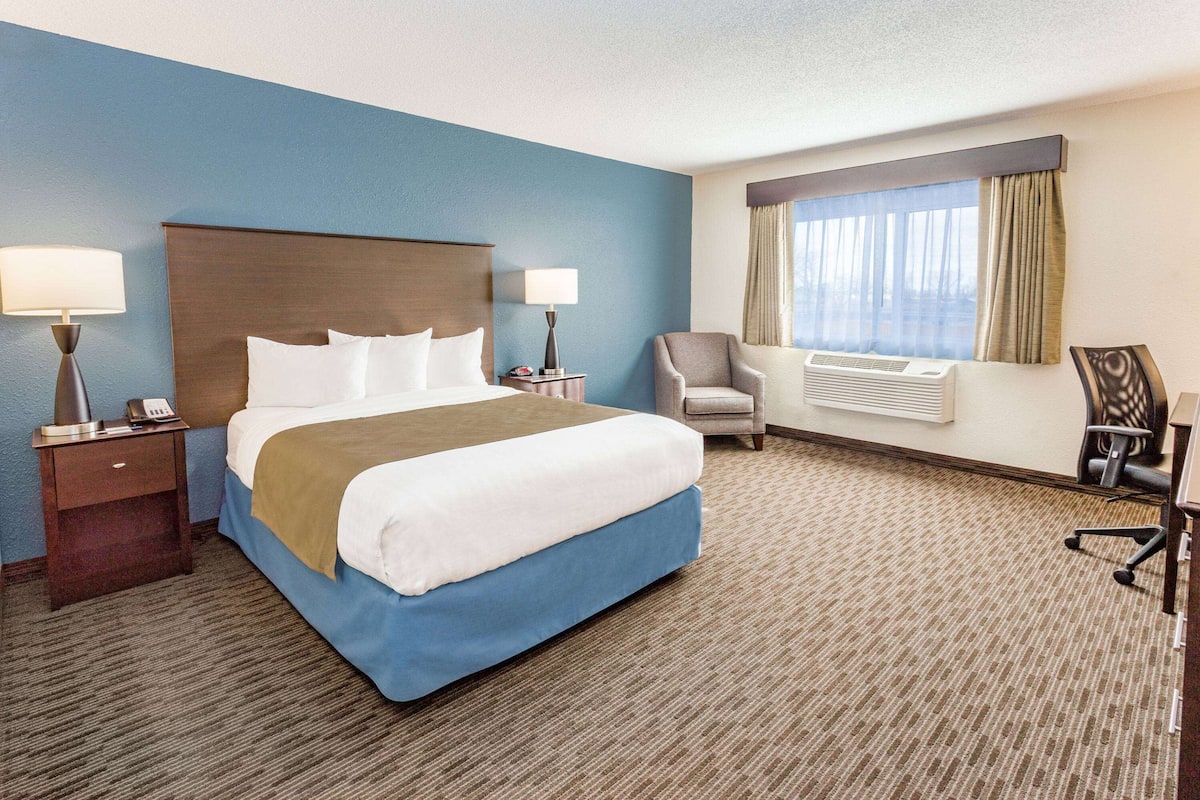 A hotel room with a large bed, two bedside tables, a chair, a desk, and a window with curtains.
