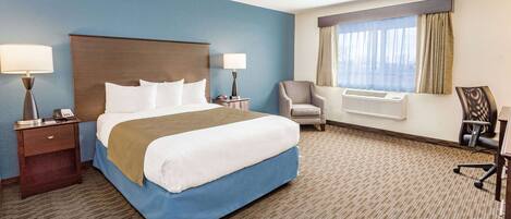A hotel room with a large bed, two bedside tables, a chair, a desk, and a window with curtains.