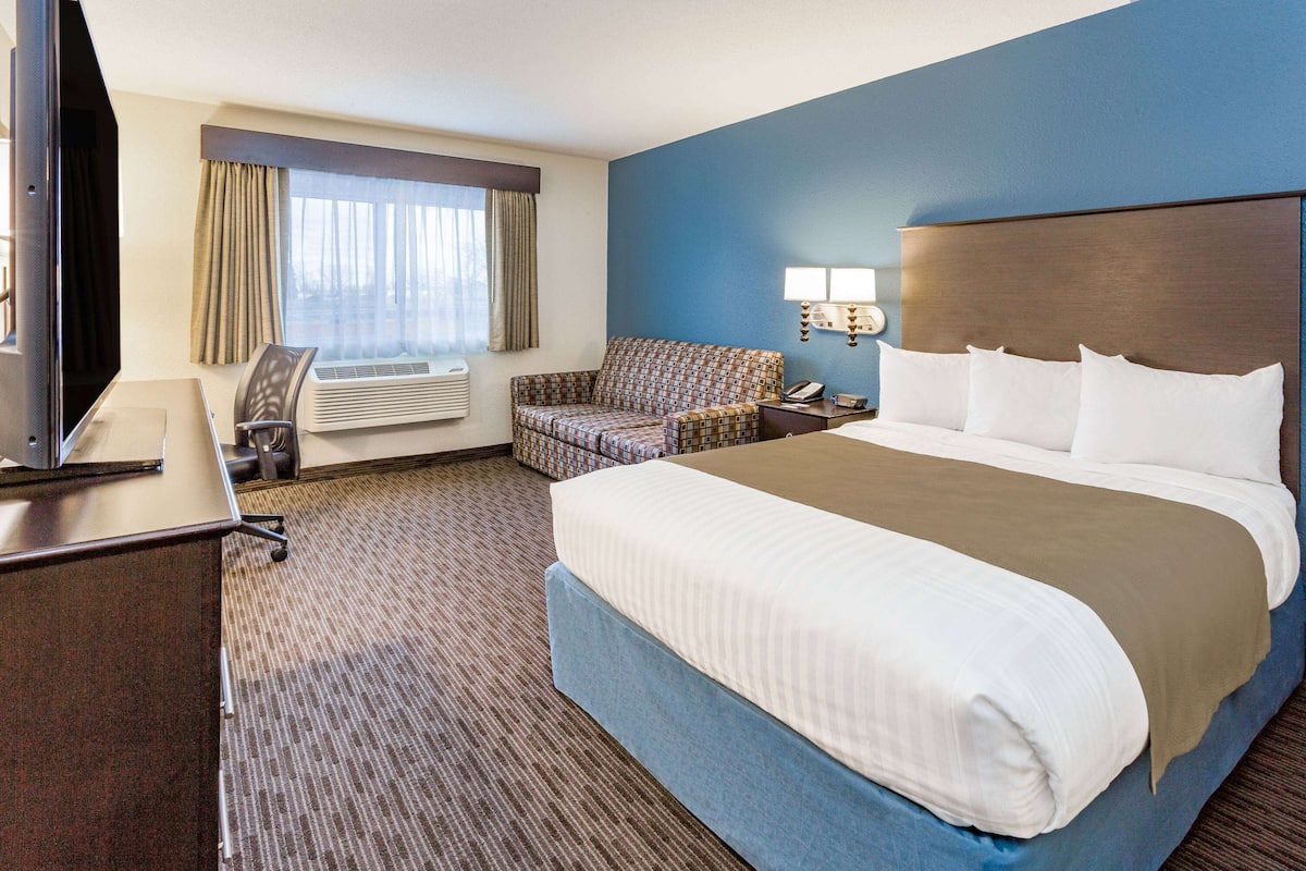 A hotel room with a large bed, a desk with a chair, a sofa, and a TV.