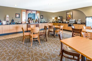 Uma sala de jantar de hotel com mesas e cadeiras de madeira, um balcão de café e um refrigerador.