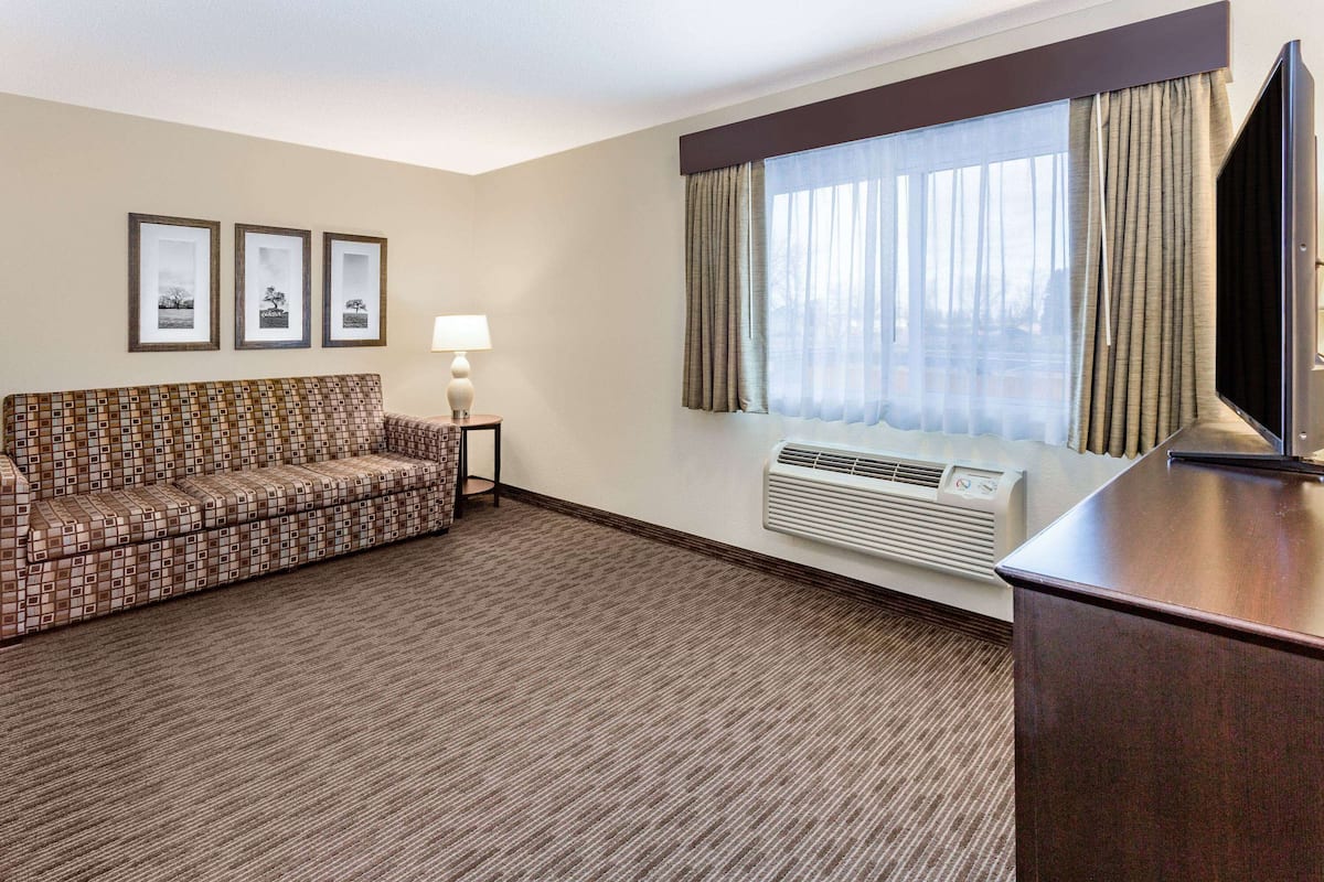 A hotel room with a patterned sofa, a flat-screen TV, a lamp, and a window with curtains.
