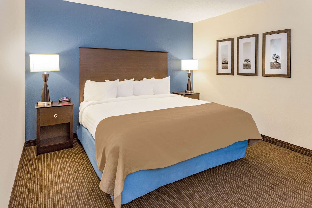 A hotel room with a large bed, two bedside tables with lamps, a blue wall, and three framed pictures on the wall.