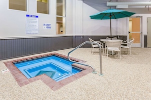 Uma pequena piscina interior para 4 pessoas, com piso de pedras e cadeiras brancas.