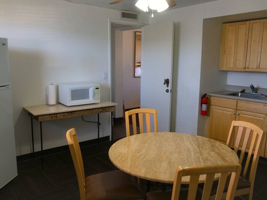 Cocina compacta con refrigerador, microondas, mesa de madera y sillas.