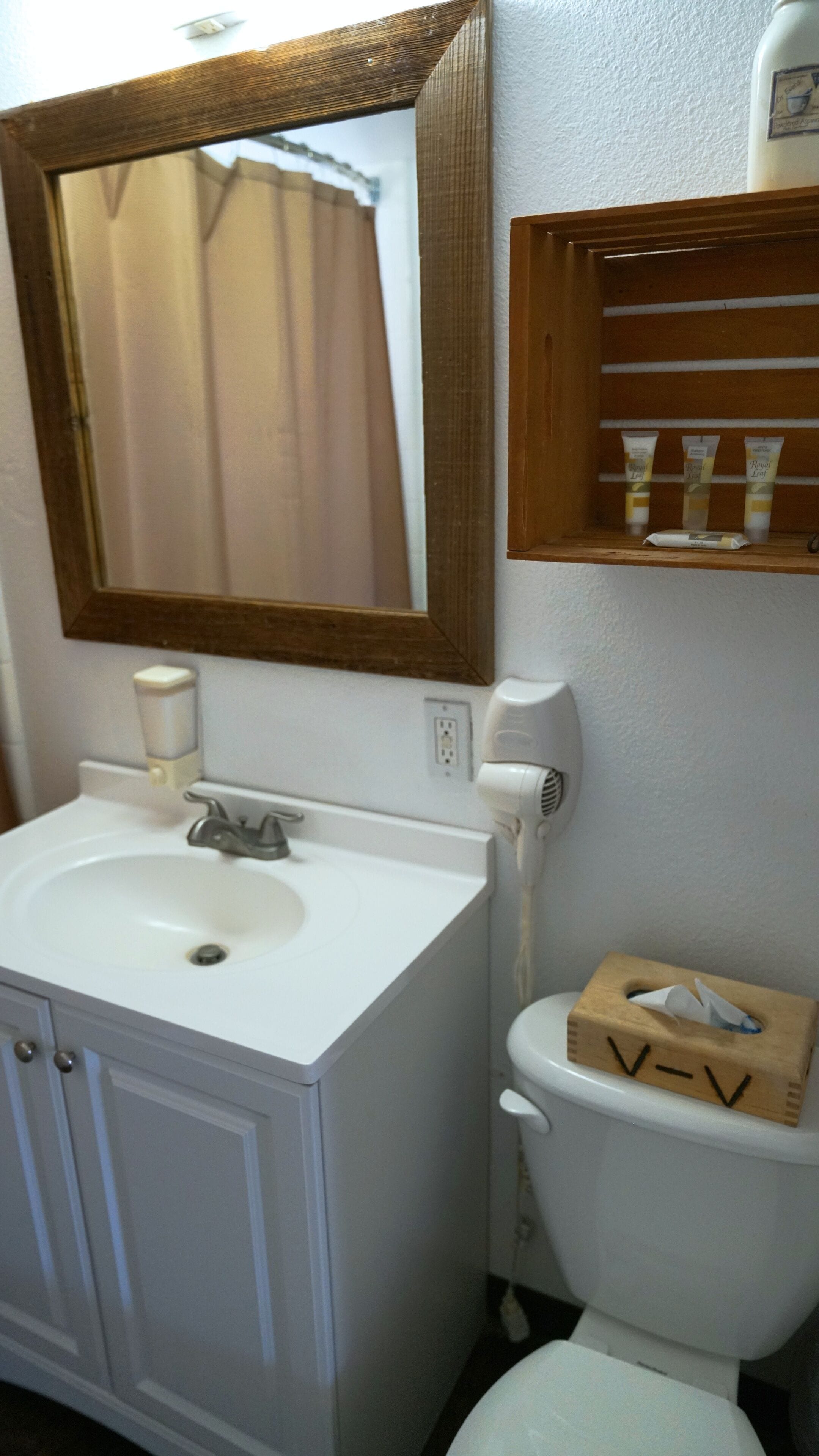A bathroom with a white sink, a mirror, a toilet, and a shelf with toiletries.