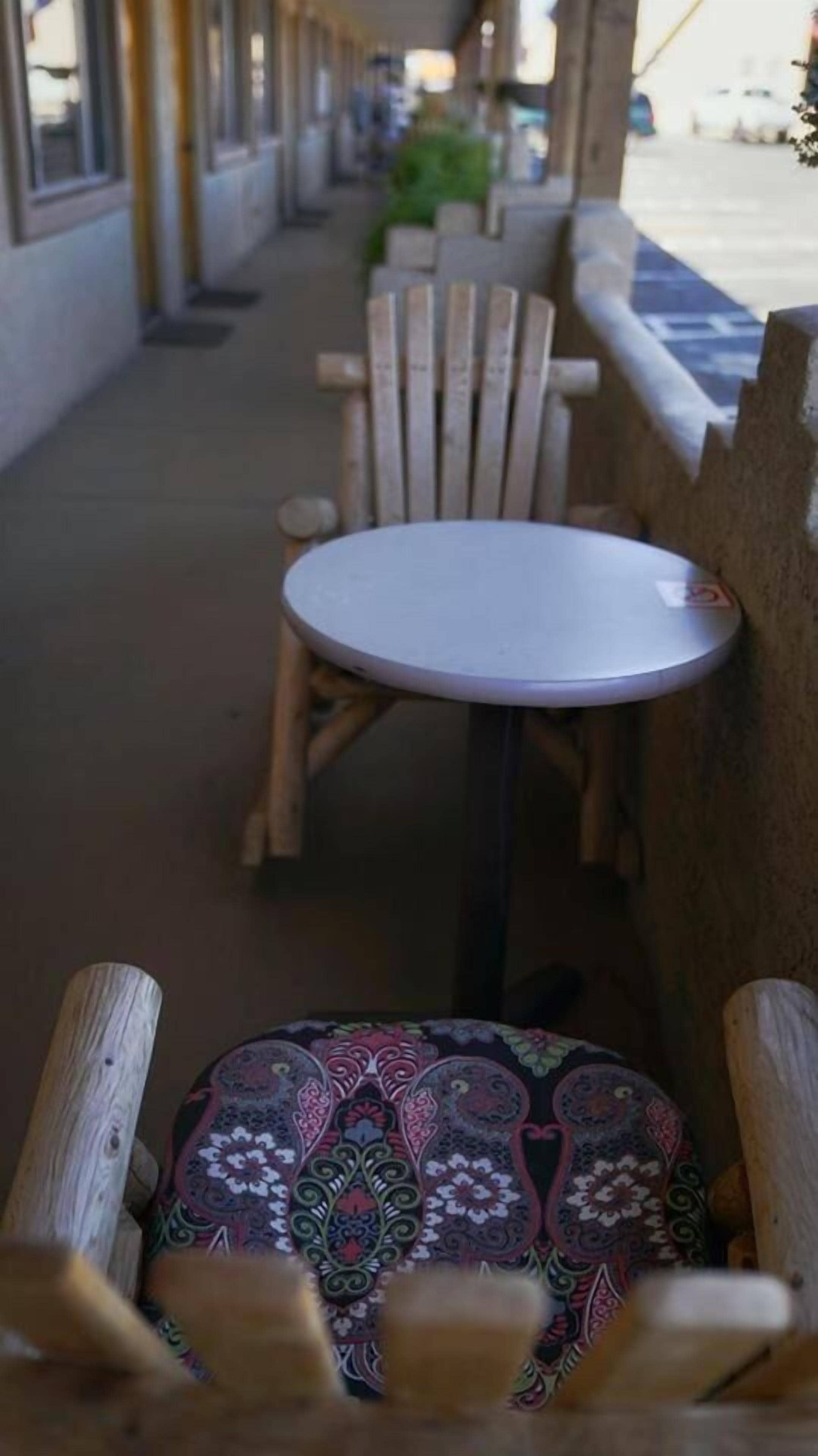 A wooden bench with a patterned cushion, a small round table, and a wooden chair in an outdoor seating area.