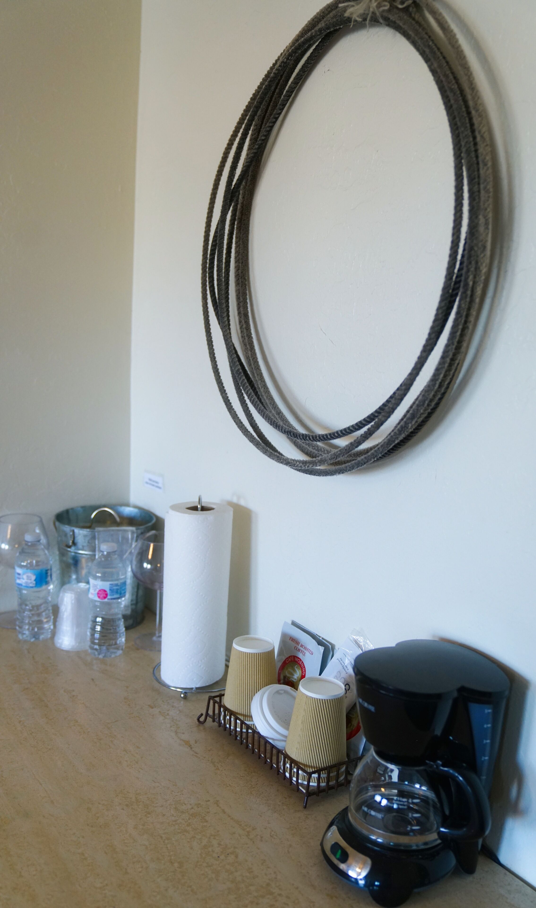 A kitchen counter with a coffee maker, paper cups, a roll of paper towels, and water bottles.