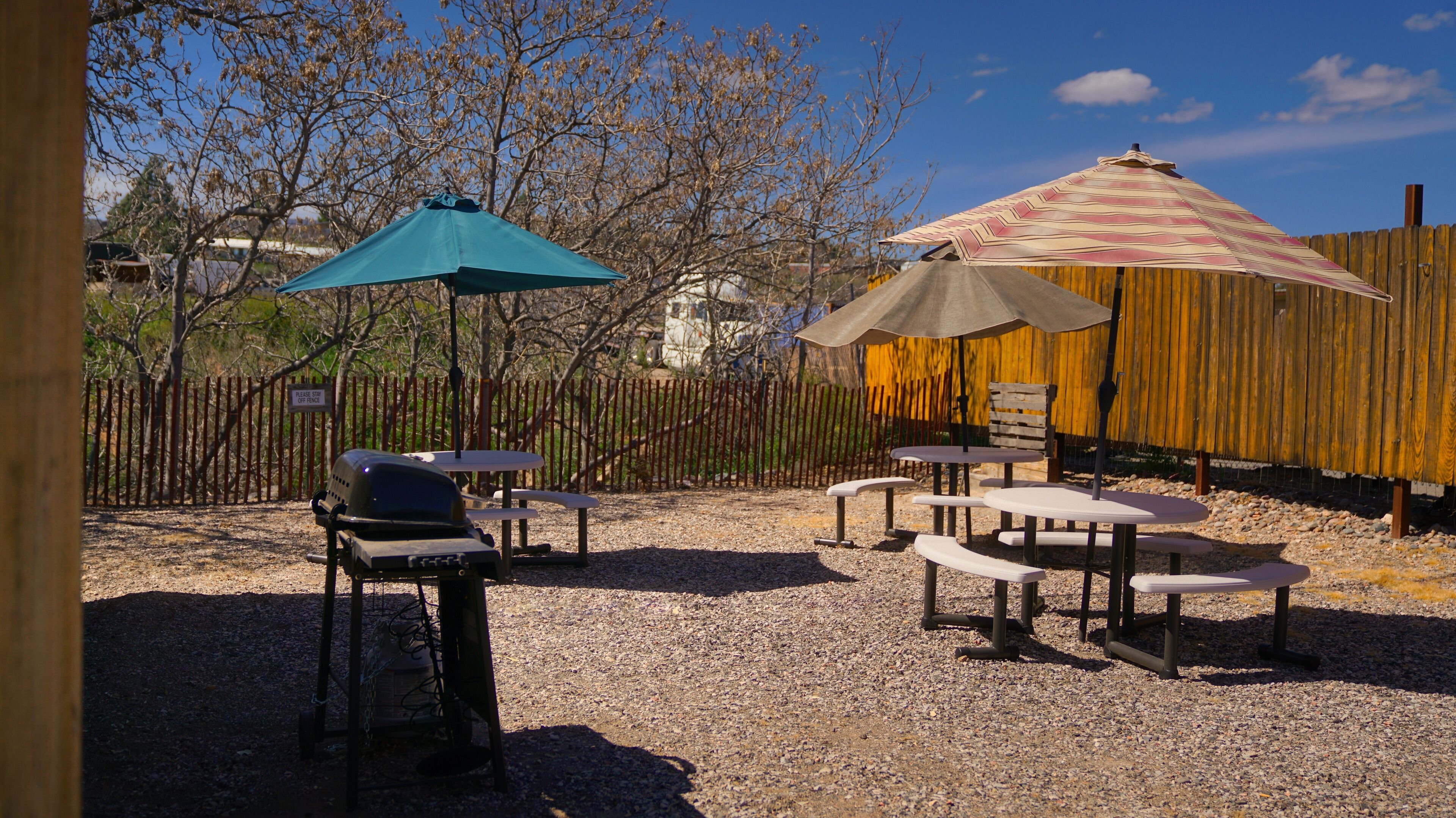 Un área de estar al aire libre con mesas, sillas, una parrilla y sombrillas que dan sombra.