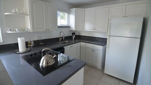 A modern kitchen with white cabinets, a black countertop, a stainless steel kettle, and a refrigerator.