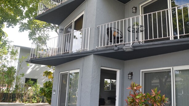 A two-story building with a balcony, large windows, and a small outdoor seating area.