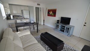 A living room with a sofa, coffee table, TV stand, and a dining area with chairs and a table.