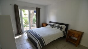 A bedroom with a bed, two bedside tables, a wardrobe, and a sliding glass door leading to a balcony.