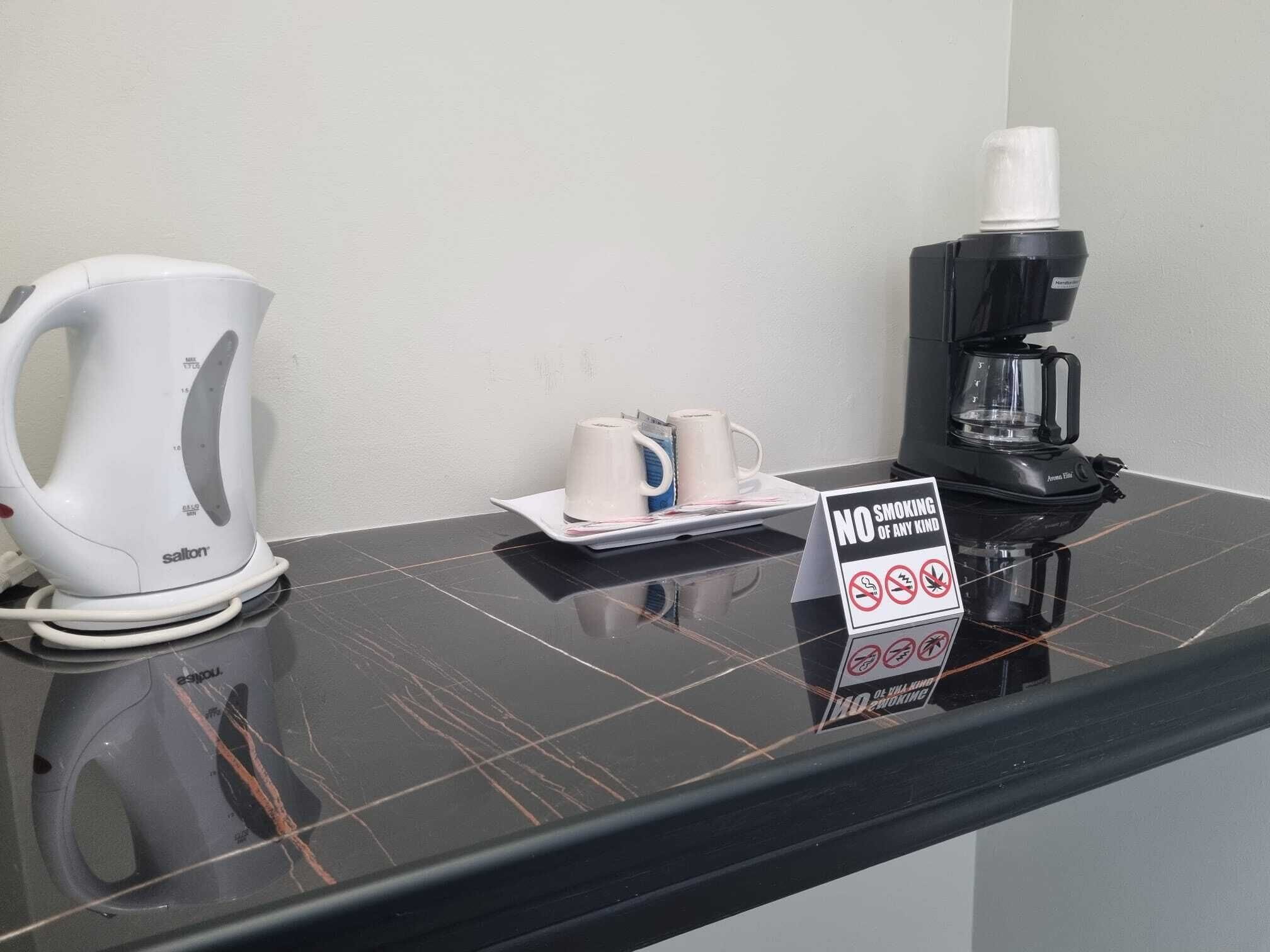 A coffee station with a kettle, coffee maker, and mugs on a black countertop.