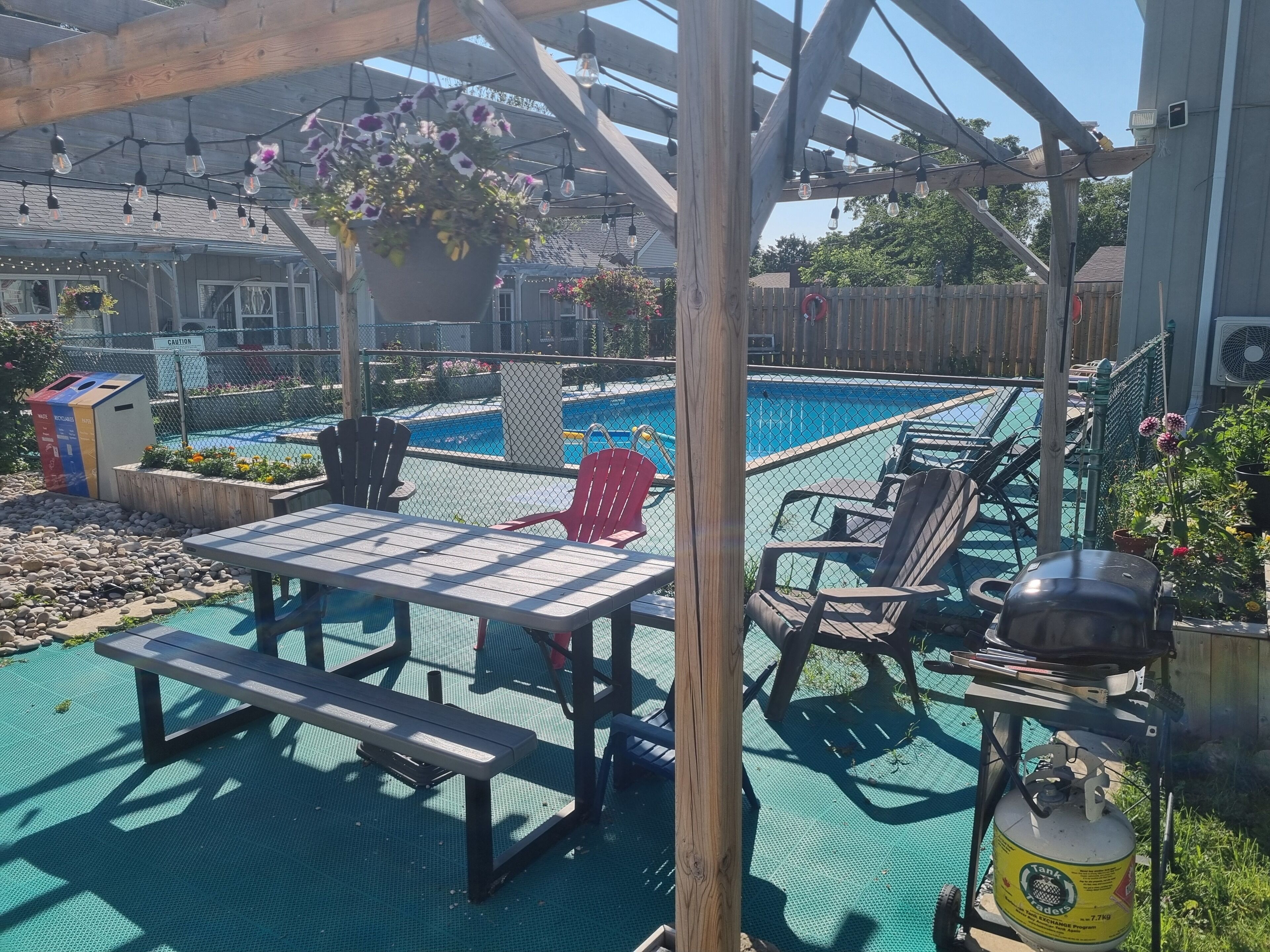 A poolside area with a table and chairs, a hanging flower pot, and a propane tank.