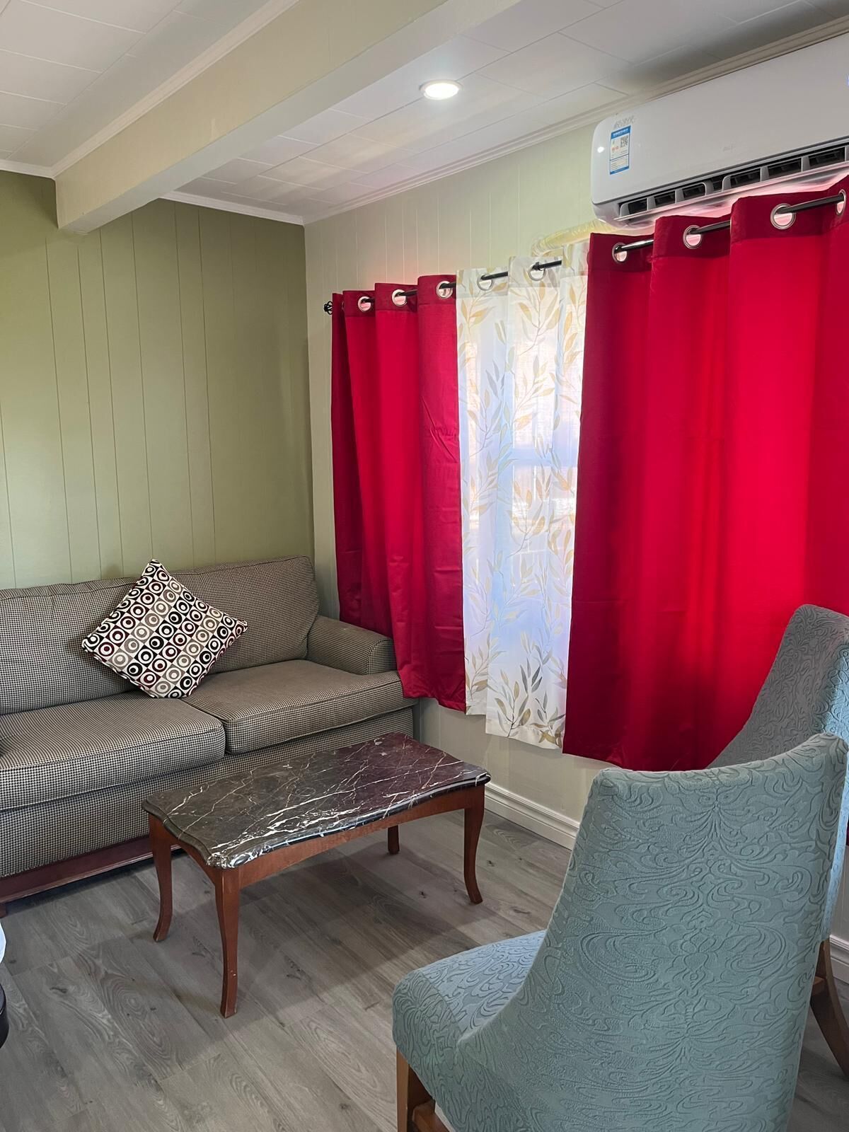 Un salon comprenant un canapé, un coussin à motifs, une table basse en marbre, un fauteuil à motifs et des rideaux rouges.