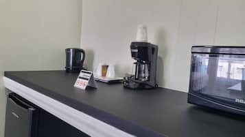 Una estación de café con cafetera, tazas y microondas sobre una encimera.