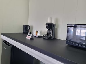A coffee station with a coffee maker, cups, and a microwave on a counter.