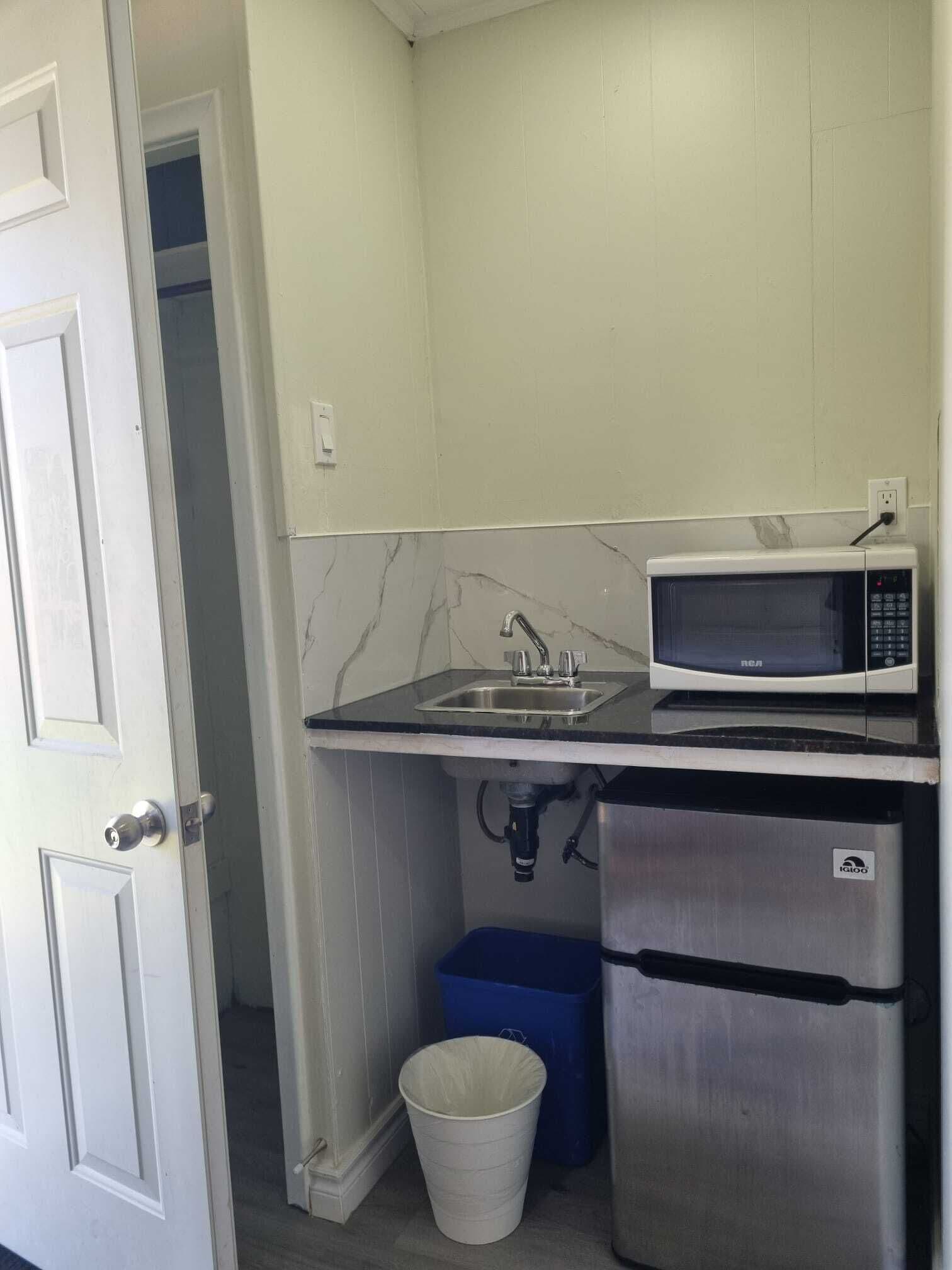 A compact kitchenette with a microwave, sink, and a small trash bin.
