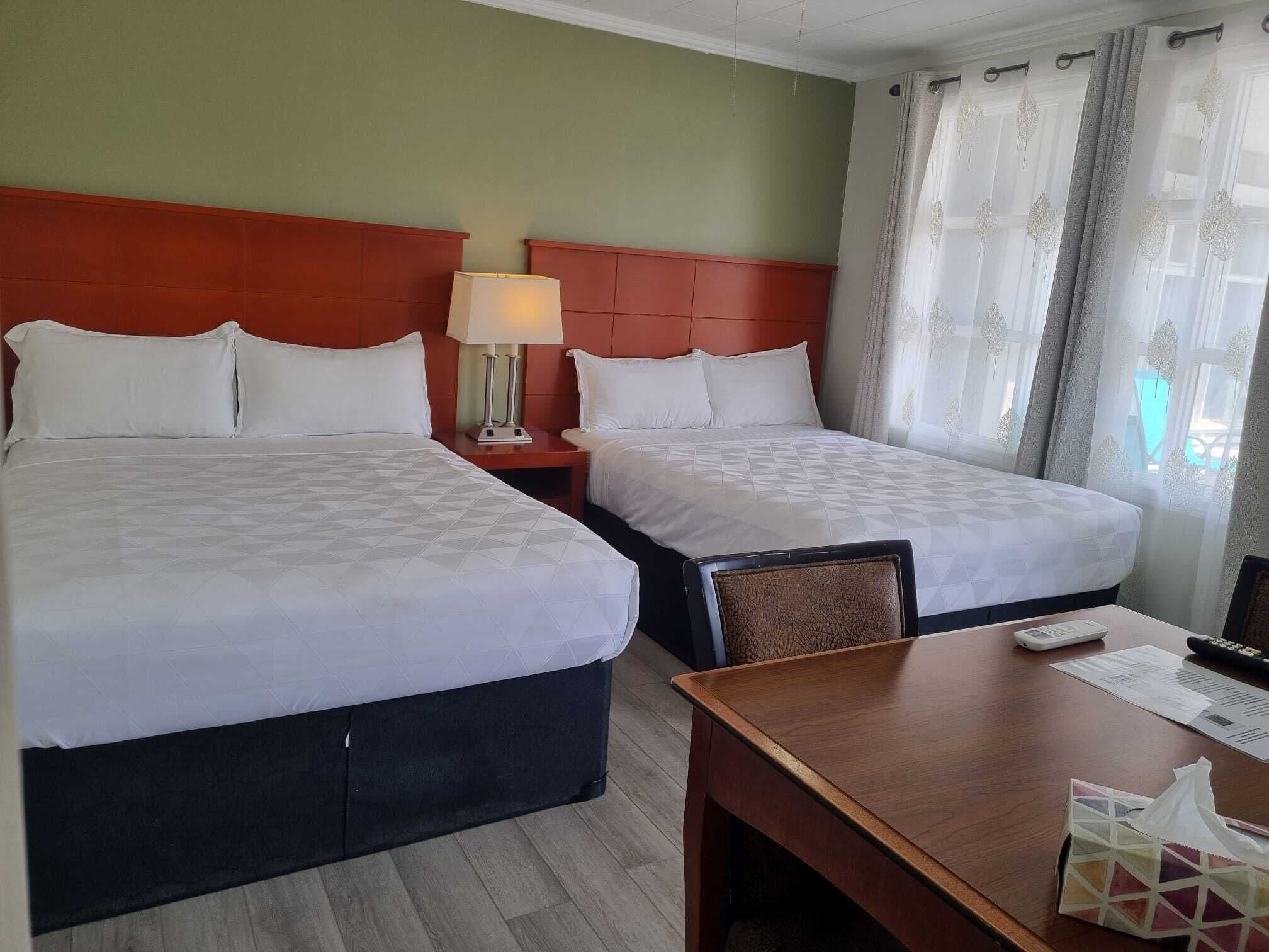 A hotel room with two beds, a bedside table with a lamp, a wooden desk, and a chair.