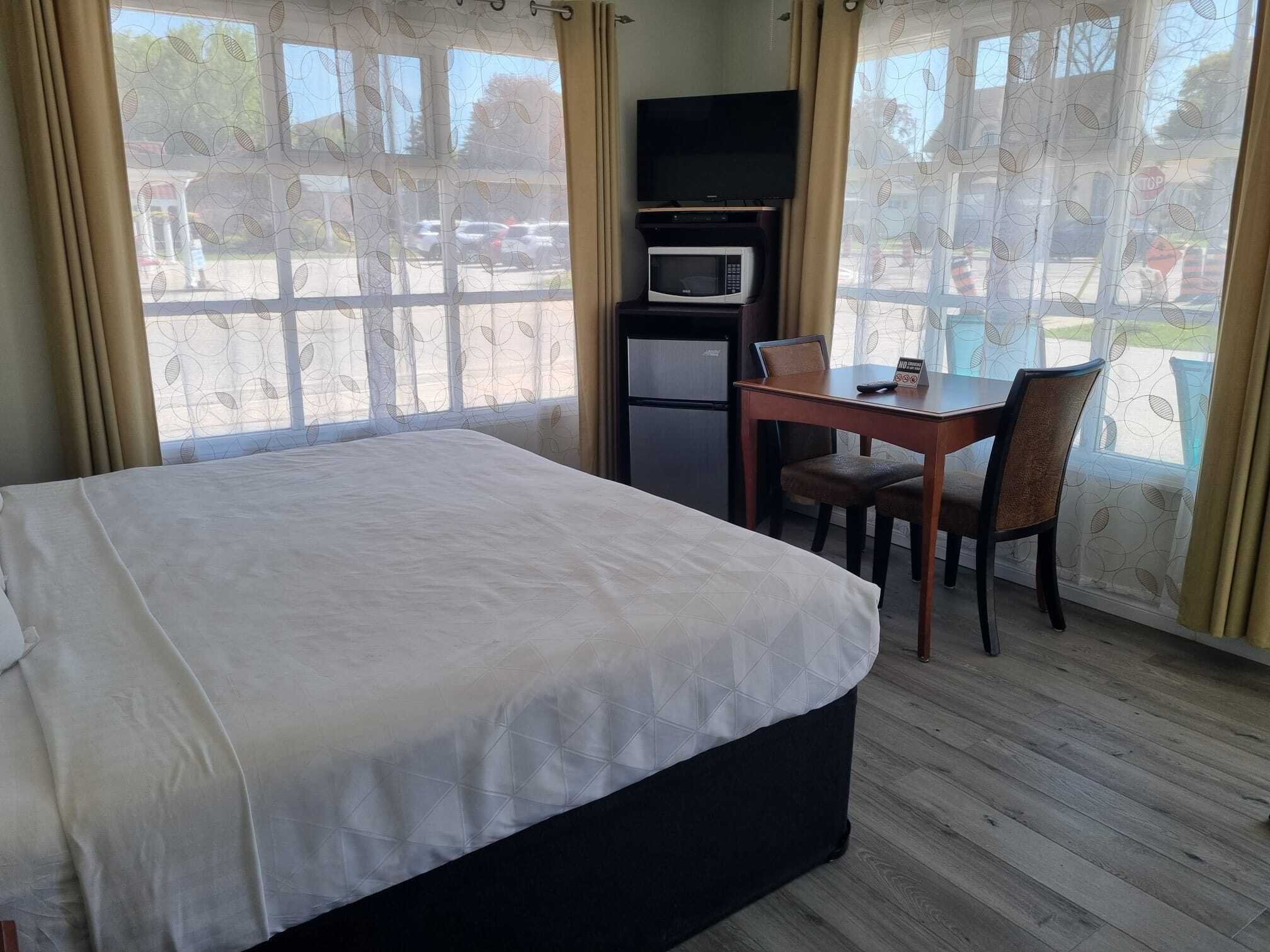 Habitación de hotel con cama, escritorio con silla, microondas y refrigerador.