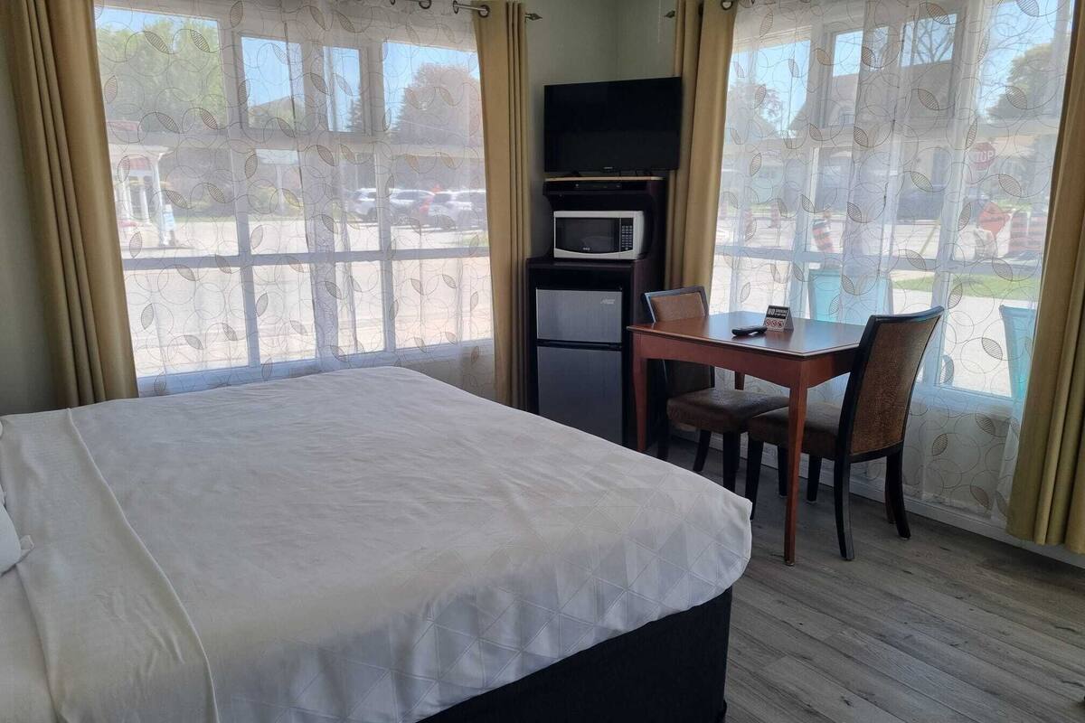 A hotel room with a bed, a desk with a chair, a microwave, and a refrigerator.