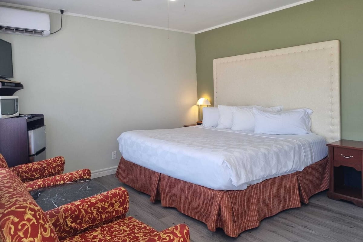 Quarto de hotel com cama, mesa com micro-ondas, ventoinha no teto e televisão.