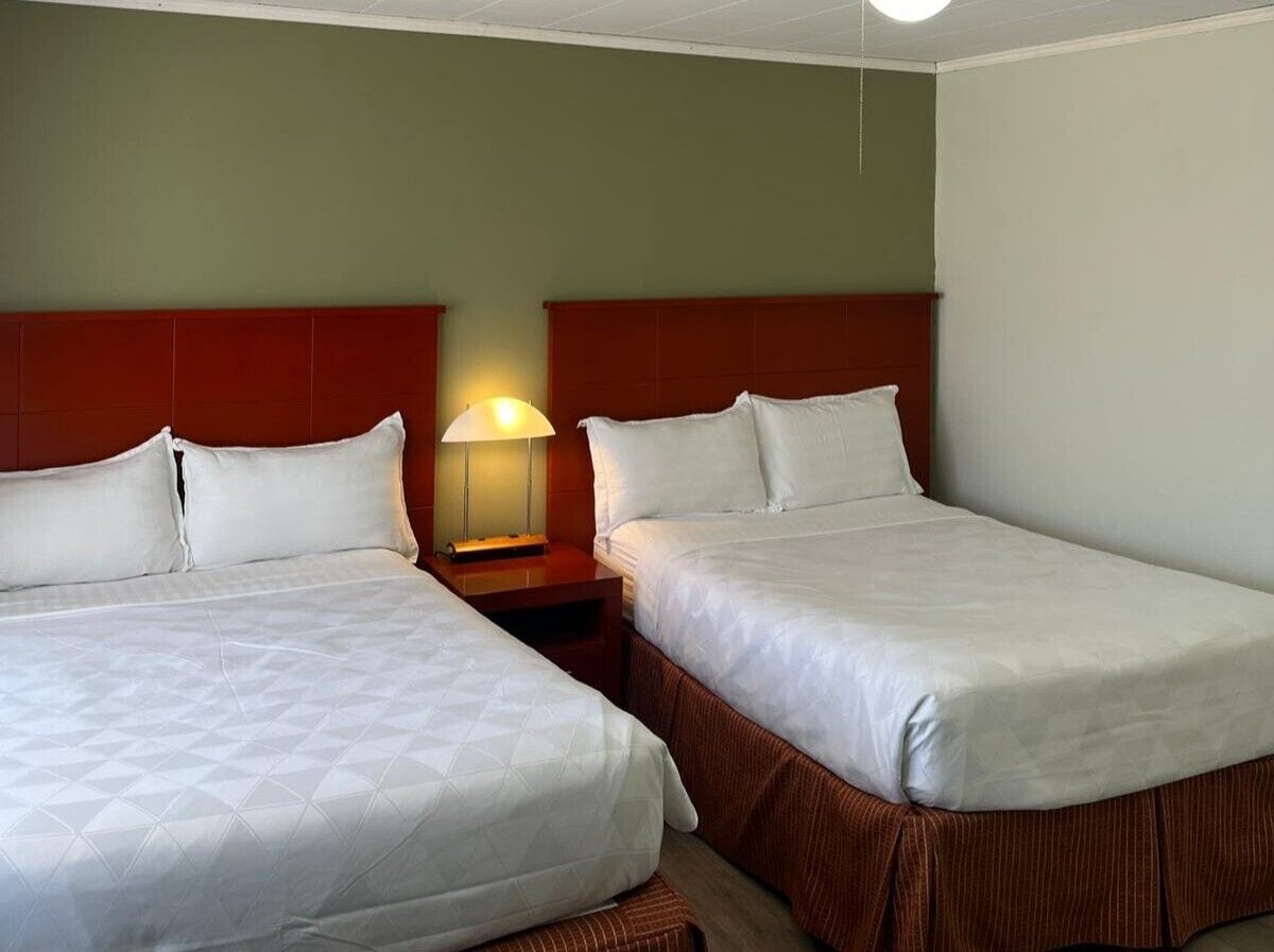 Une chambre d’hôtel avec deux lits, une table de chevet avec une lampe et une tête de lit rouge.