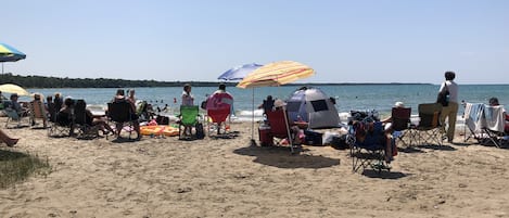 Una playa con gente relajándose bajo sombrillas, una carpa y sillas de playa.